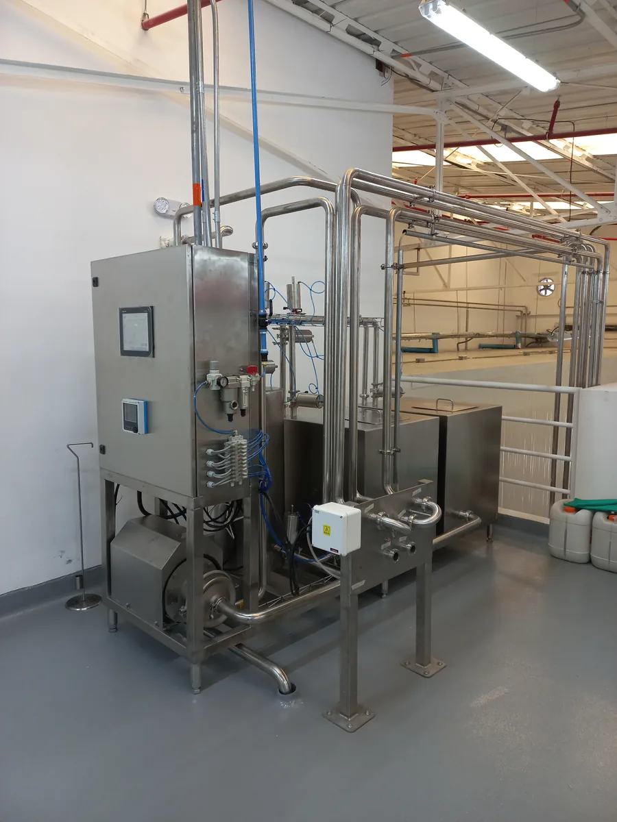 Skid de proceso en acero inoxidable con su panel de control, tuberías sanitarias y bomba, instalado en una sala de producción
