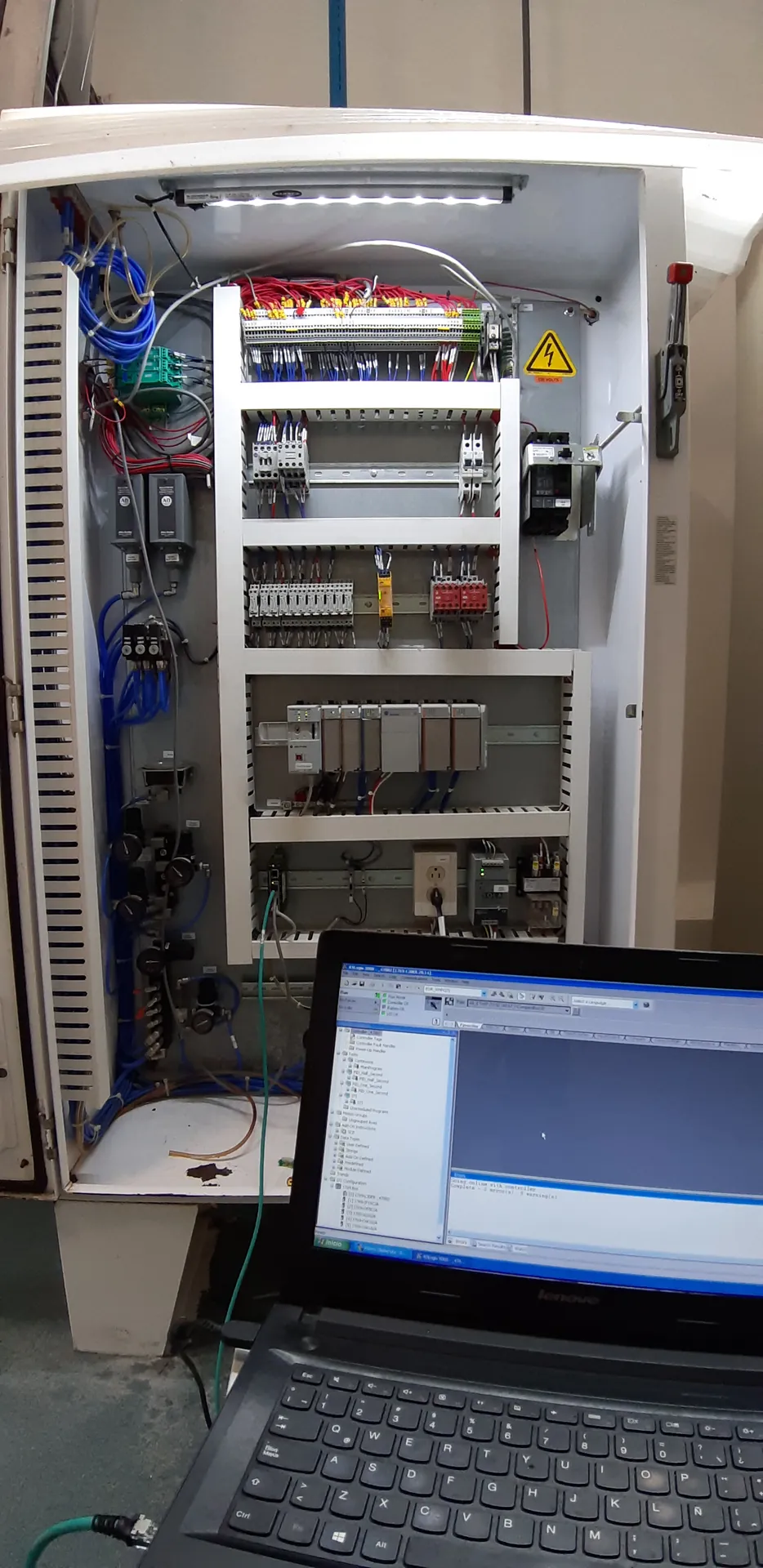 Tablero de control abierto durante la puesta en marcha, con un portátil conectado al PLC para cargar el programa