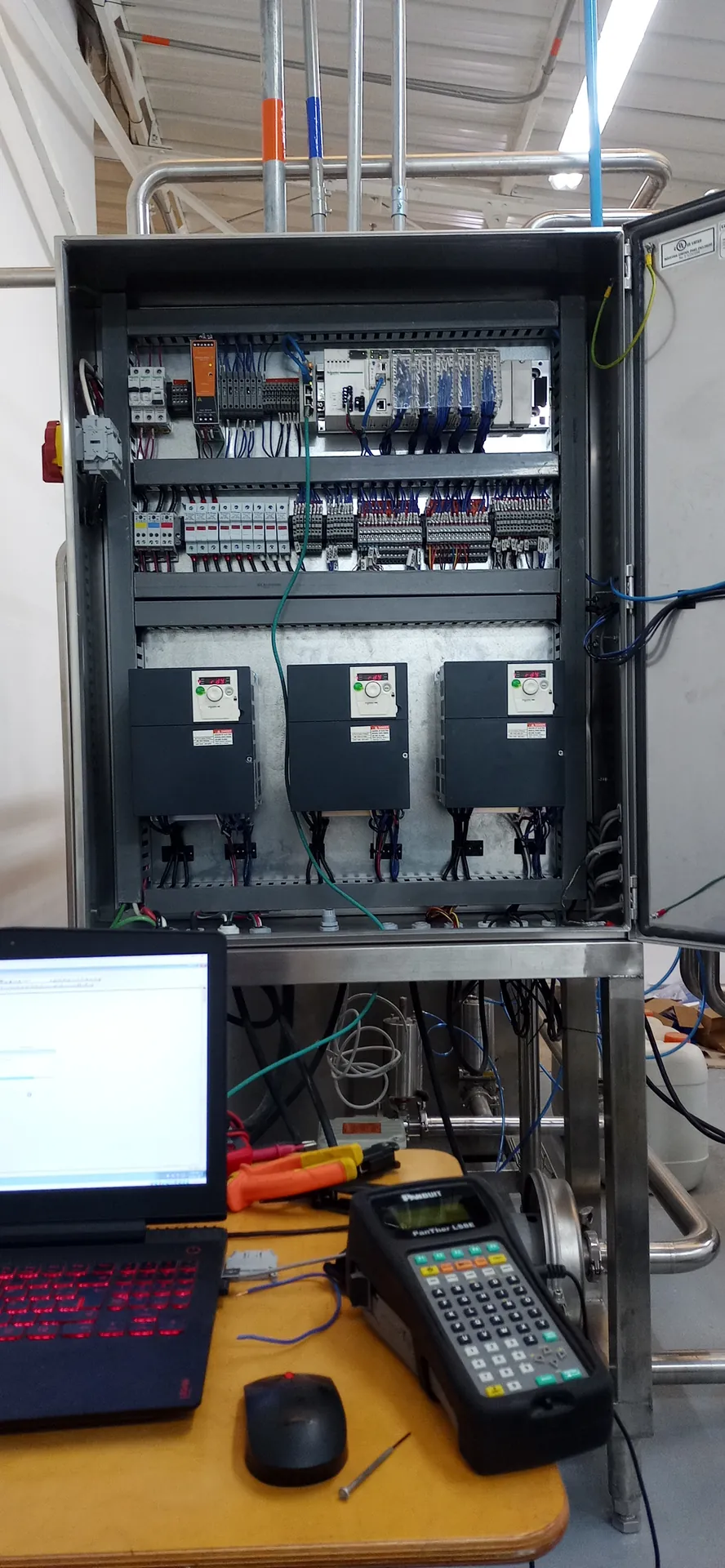 Puesta en marcha de un tablero en acero inoxidable con tres variadores de velocidad, con el portátil y el terminal de pruebas sobre la mesa