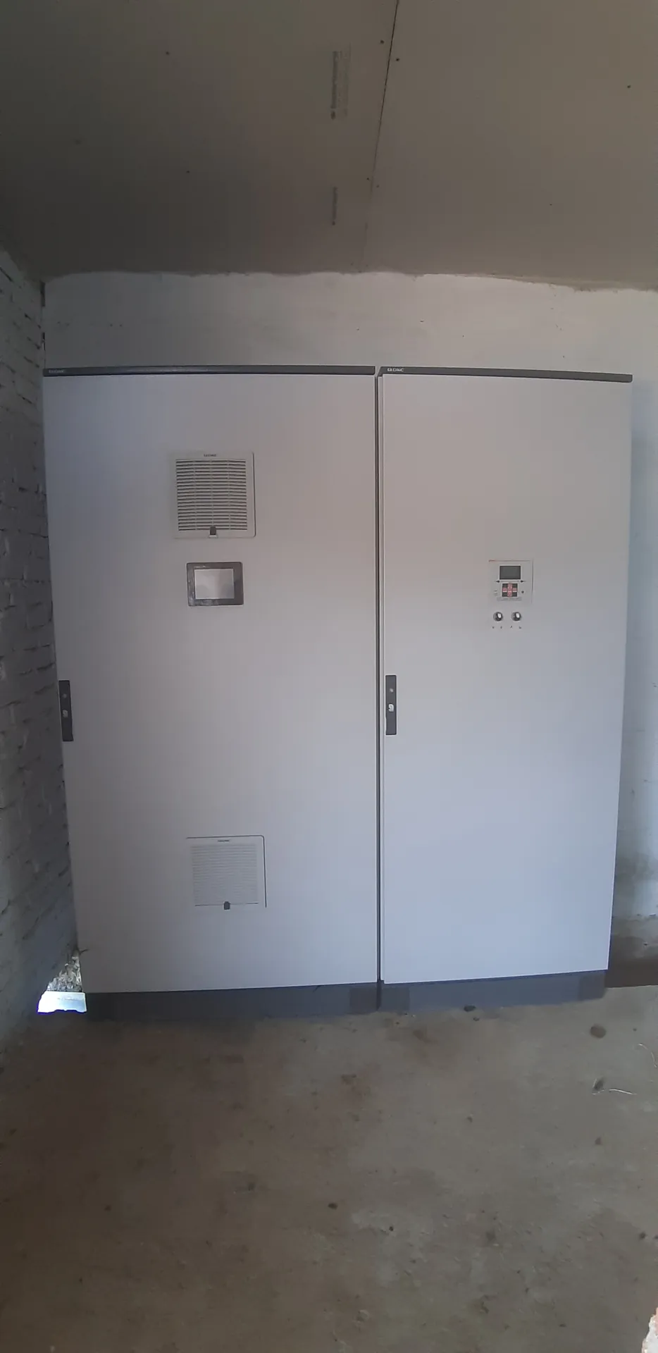 Dos tableros cerrados instalados en un cuarto eléctrico, con ventilación forzada y panel de medición en la puerta