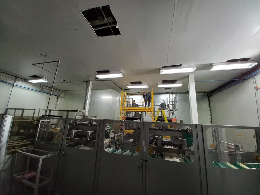 Dos técnicos sobre un andamio instalan equipos en el techo de una sala con paneles aislantes y difusores