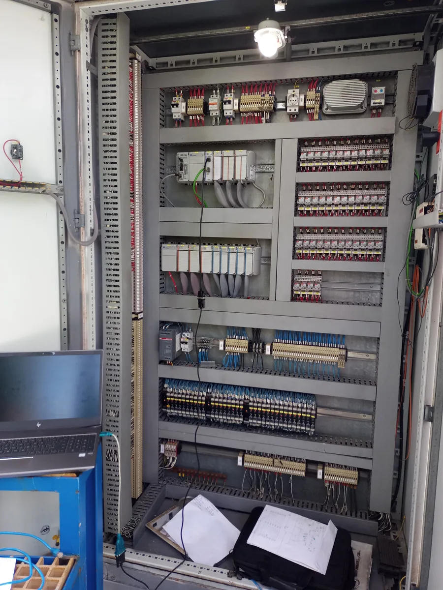 Tablero de gran formato con PLC modular, bancos de relés de interposición y borneras, con los planos abiertos durante el montaje